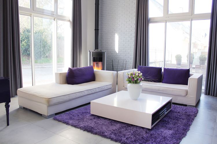 Бежевый диван в интерьере: гостиная с белыми кирпичными стенами и диваны с тёмно-фиолетовыми подушками и ковром